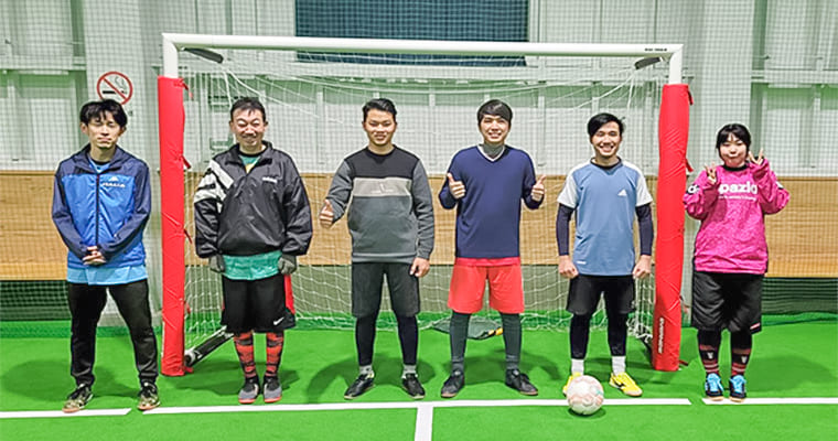 サッカーゴールを前に、6人のメンバーが笑顔で立っている様子